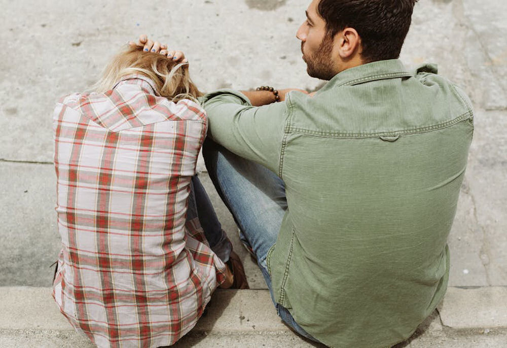 Woman holding head next to concerned man while sitting on concrete steps