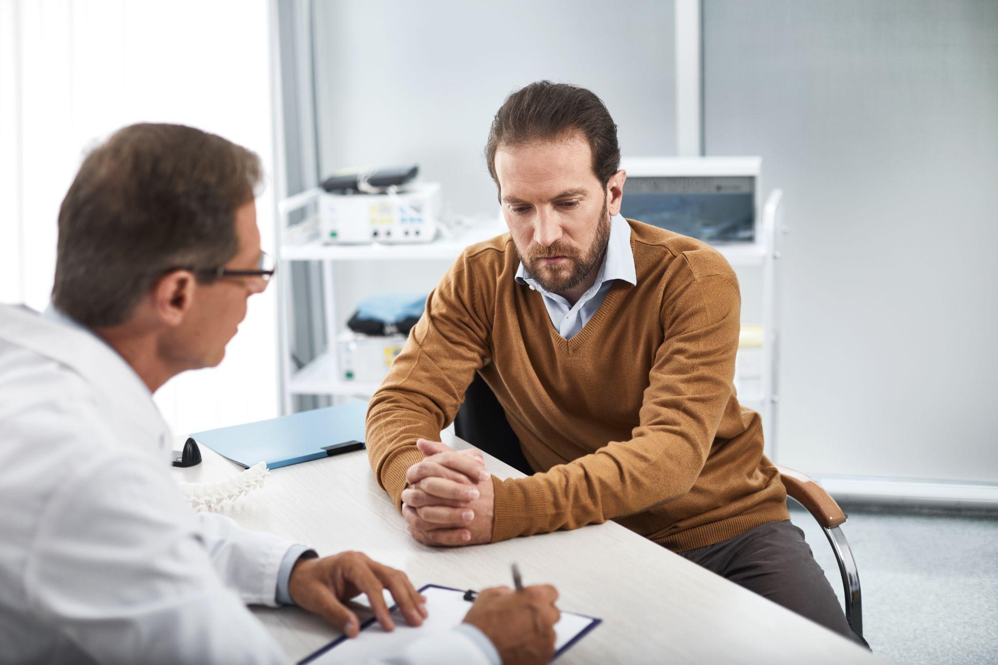 doctor speaking with bearded man in his office while recording necessary data on paper