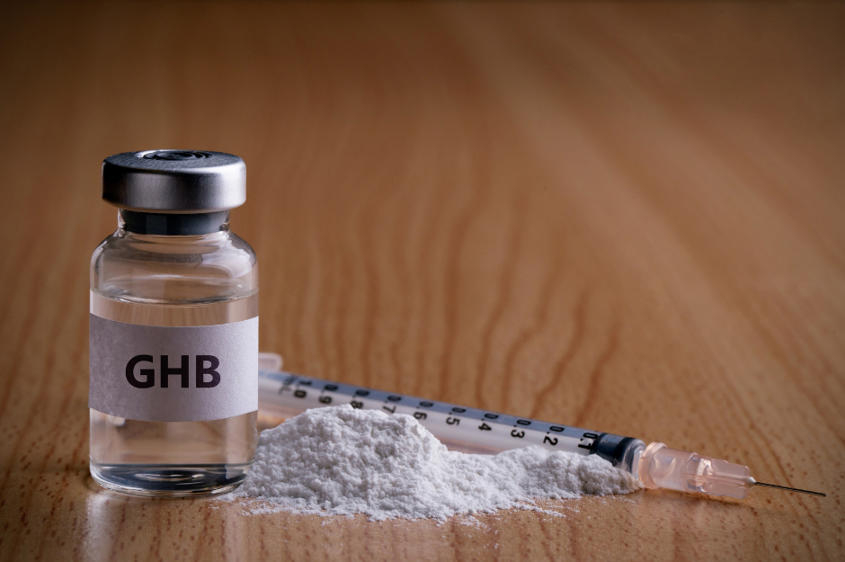 Bottle of GHB with drug powder and injection needle on wooden background