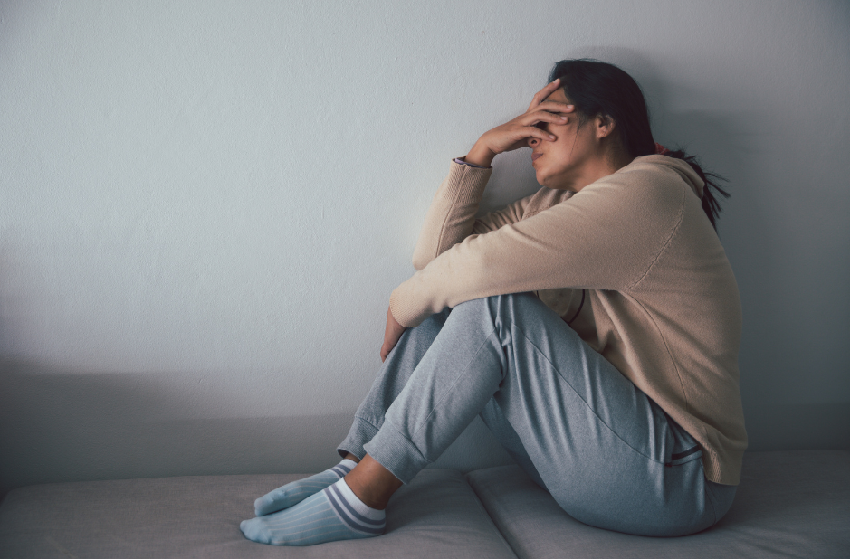 Depressed woman sitting against floor at home with dark room feeling miserable