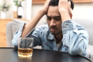 Man looking distressed while looking at a glass of whiskey