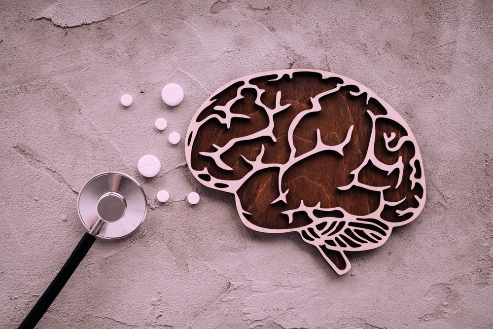 Wooden brain model beside a stethoscope and pills