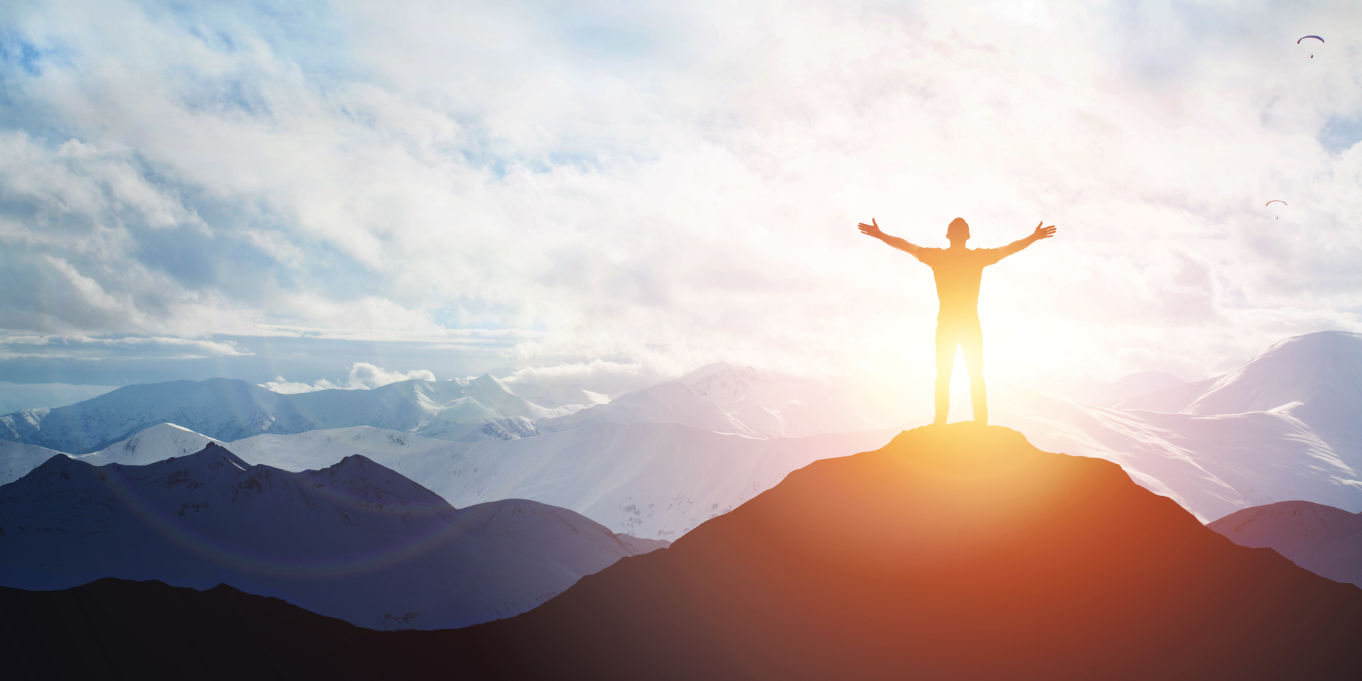 Man standing triumphantly on the top of a hill during sunrise