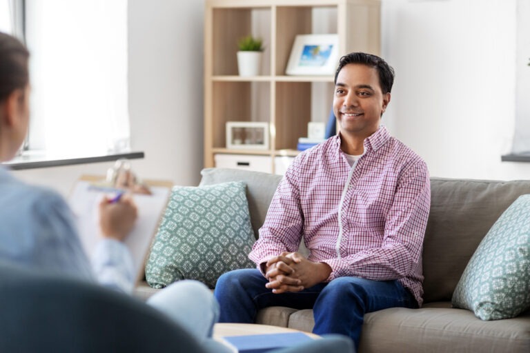 Happy man discussing depression and addiction treatment with therapist using clipboard.