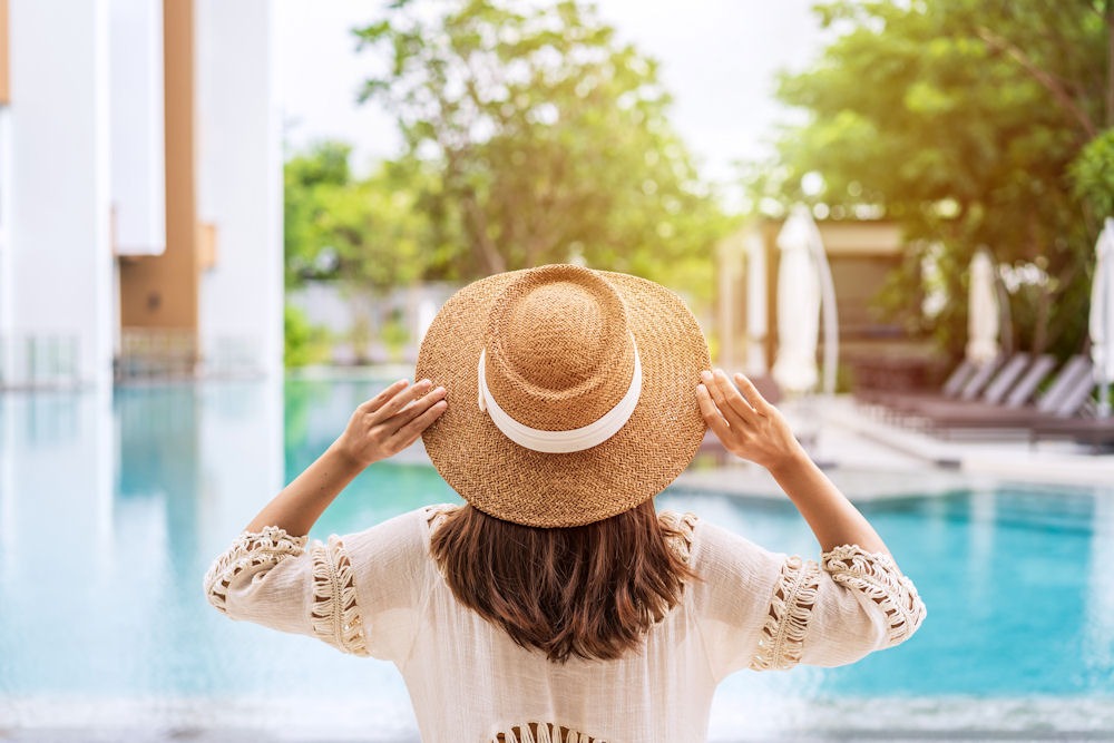 Back view of a woman adjusting hat while relaxing by pool