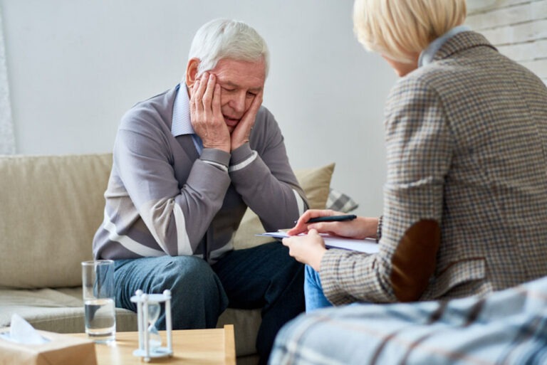 Sad man holding head while talking with counselor