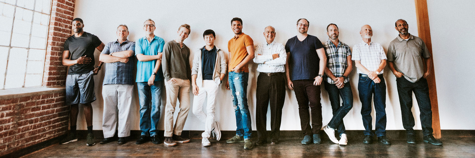 Row of men of diverse appearances lining up against a wall